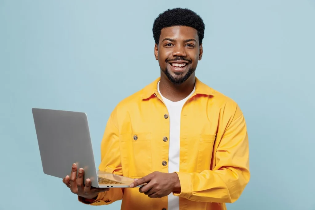 Happy African American man standing looking at camera while smiling and holding laptop